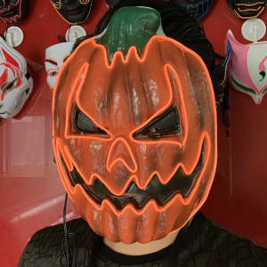 A pumpkin-shaped mask with an angry expression, featuring bright orange and green colours, illuminated with LED lights.
