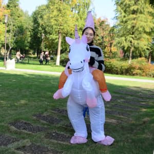 An inflatable unicorn costume in white and pink, worn by a person in a park setting, featuring a party hat.