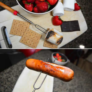 A telescopic barbecue fork with a red handle, shown with roasted marshmallows, strawberries, chocolate, and crackers.