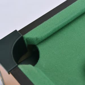 A close-up view of a mini billiard game's green felt surface and pocket, with a black frame. It features a logo.