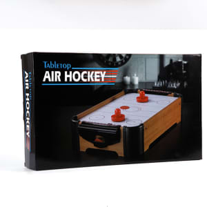 A tabletop air hockey game in a box, featuring a wooden design and red pucks. The packaging has a logo.