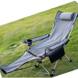 A grey camping lounge chair with a headrest and side pocket on a grassy surface. It has a frame for support.