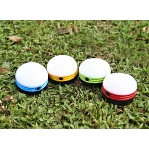 Four portable camping lights in blue, yellow, green, and red, placed on grass. Each light has a circular design.