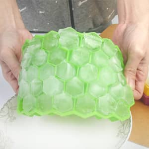 A green silicone ice cube tray with hexagonal shapes is being held, filled with ice cubes.