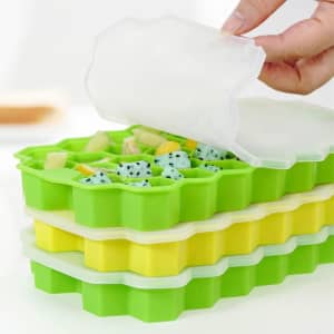A silicone ice cube tray with lids in green and yellow, filled with various frozen fruits.