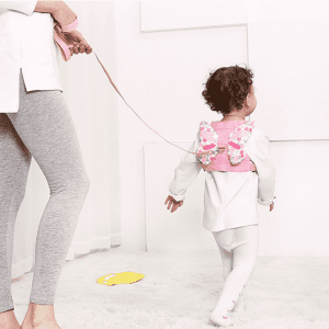 A pink child anti-lost back strap with butterfly wings, attached to a parent, assisting a toddler walking.