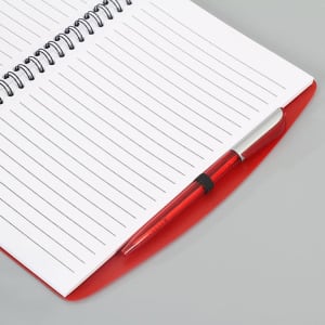 A red spiral notebook with lined pages, accompanied by a matching red pen. It features a logo on the cover.