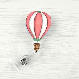 A pink and white hot air balloon badge holder clip with a clear attachment. It features a decorative design.