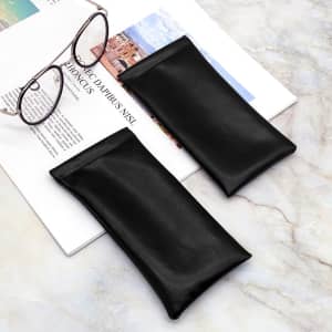 Black PU eyeglass pouches displayed alongside a pair of glasses on a marble surface, with a magazine underneath.