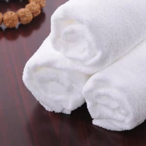 White rolled bath towels stacked on a wooden surface, beside a decorative bead bracelet.