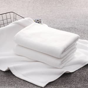 A stack of white bath towels neatly arranged on a soft surface, alongside a wire basket.