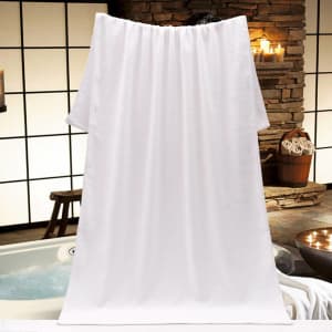 A large white towel hangs against a background of stone walls and a bath setting, featuring soft lighting and decorative candles.