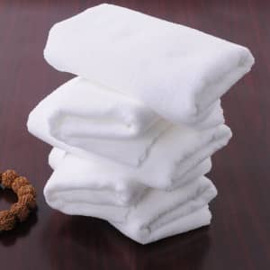 A stack of four white bath towels neatly folded on a wooden surface, accompanied by a decorative item.
