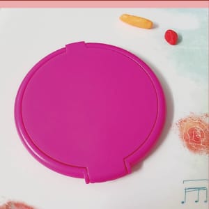 A round, pink folding mirror with a secure clasp, placed on a surface with colourful candies nearby.