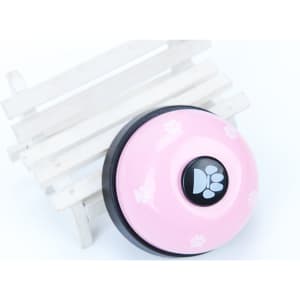 A pink pet training bell with a black centre, featuring paw print designs, placed on a white wooden stand.