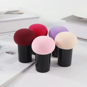 A set of five Mushroom Head Powder Puffs in colours including burgundy, pink, purple, and beige, housed in black holders.