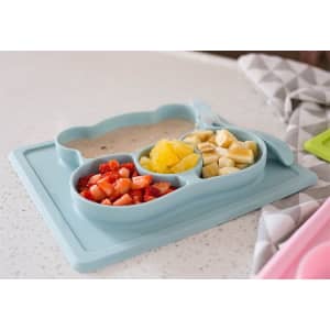 A blue, non-slip children's plate with three sections, holding strawberries, bananas, and pineapple on a countertop.