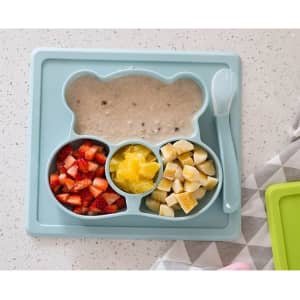 A blue non-slip children's plate shaped like a bear, featuring sections for fruit and porridge, with a matching spoon.