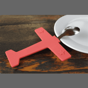 A pink airplane-shaped fork and spoon set rests next to a white plate on a wooden surface.