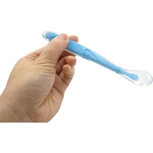 A baby training spoon in blue held by a hand, featuring a transparent tip and a logo on the handle.
