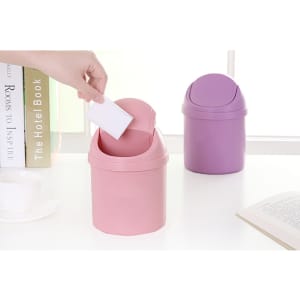 A pink and a purple mini trash can are displayed on a table, with a hand dropping a piece of paper into the pink one.