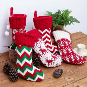 A collection of red and white Christmas stockings with various festive patterns, placed on a wooden surface surrounded by pine cones.