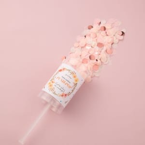A clear container filled with pink and peach confetti, featuring a label and a straw.