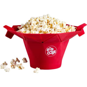 A red popcorn bucket filled with popcorn, featuring a logo and some spilled popcorn kernels around it.