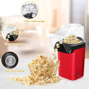 A red hot air popcorn maker with a clear top, measuring spoon, and freshly popped popcorn in a bowl.