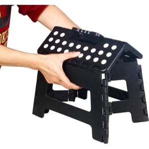 A black 11-inch folding step stool with a handle and holes for grip, being held by a hand.
