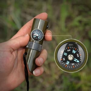 A green camping whistle with a compass attached, held in a hand against a natural background.