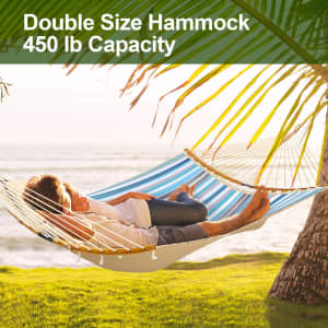 A double hammock in blue and white quilted fabric, suspended between trees near the ocean, with two people relaxing.