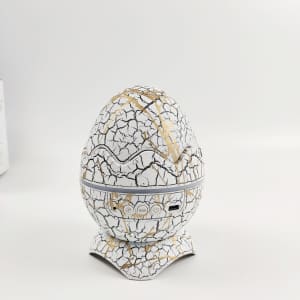 A cracked white and gold egg-shaped projector with buttons at the base sits on a flat surface.