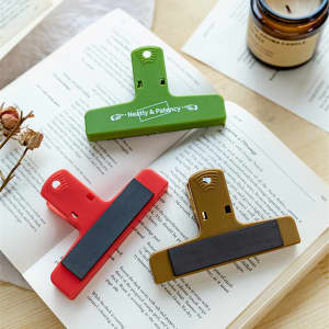 Three magnetic plastic clips in green, red, and brown lying on an open book, with a candle in the background.