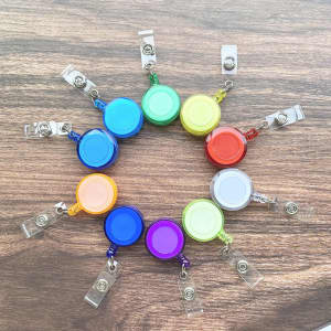 A circle of colourful retractable badge holders displayed on a wooden surface, featuring various hues including blue, red, and green.