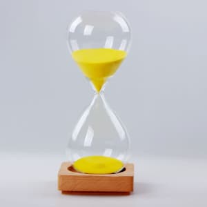 A clear glass sand timer with yellow sand, set on a wooden base.