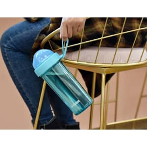 A drink bottle in turquoise with a compartmentalised double drinking straw, held by a person sitting on a gold chair.