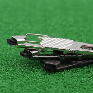A multi-functional 7-in-1 golf tool in silver and black on a green turf background, featuring various brushes and tools.