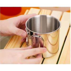 A stainless steel camping mug with a folding handle, displayed on a wooden surface. The mug is shiny and metallic.