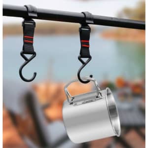 A stainless steel camping mug with a folding handle, suspended from hooks by straps against a blurred outdoor background.