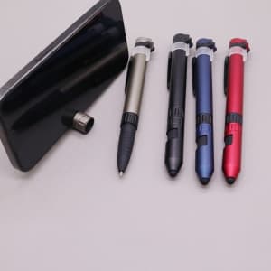 A smartphone with a phone stand beside four multi-tool pens in silver, black, blue, and red. Each has a logo.