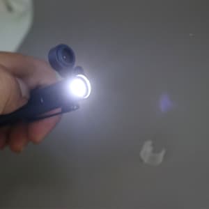 A black multi-tool pen with an LED light at the tip, being held in a hand.