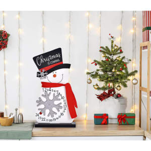 A festive snowman calendar ornament in white, with a black hat, red scarf, and a snowflake design.