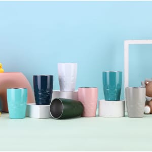 A collection of 11 oz. travel tumblers in various colours including teal, navy, pink, white, and grey, displayed on white pedestals.
