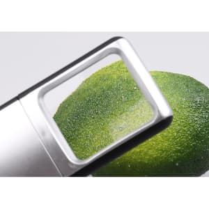 A silver slide-out magnifier with light focusing on a green fruit, likely an avocado. It features a logo.