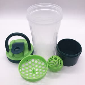 A drink bottle with a transparent body, green lid, and accessories including a storage container and mixing ball.