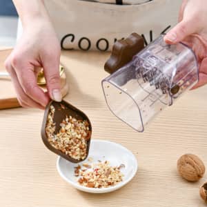 A manual mashing and grinder in transparent plastic, featuring brown accents, with chopped ingredients being poured into a bowl.