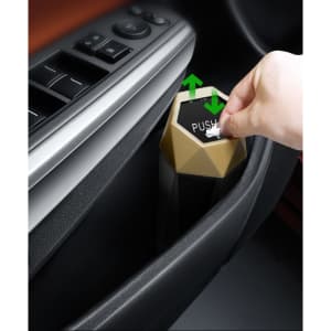 A hexagonal, metallic car trash can with a push lid, featuring black and gold colours, being interacted with by a hand.