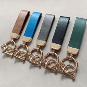 A set of five car keychains in brown, blue, grey, black, and green, featuring a circular gold attachment.