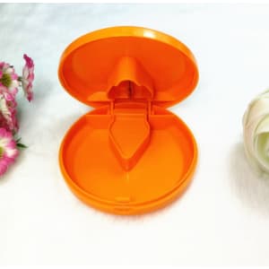An orange plastic pill cutter and box, featuring a hinged lid and a compartment for pills, set against a soft background.